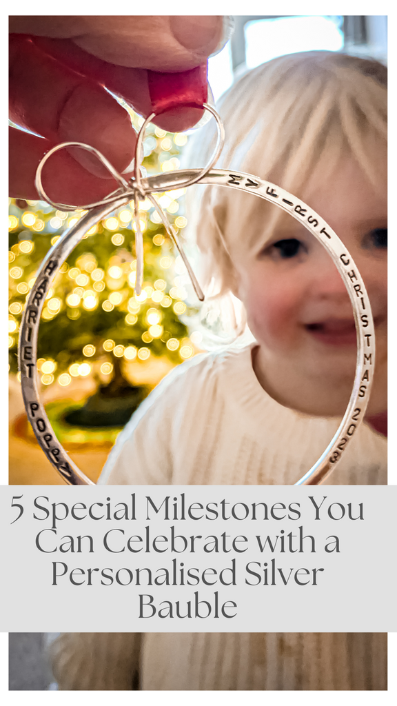 Personalised silver bauble on the tree in the foreground with young child blurred in the background — celebrating baby’s first Christmas