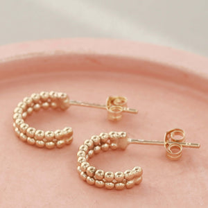 Small 9ct gold hoop earrings arranged on a pale pink dish as a delicate gift for bridesmaids or brides.