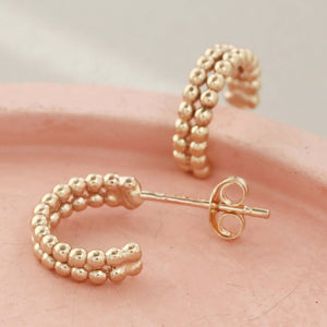 Detailed image of 9 carat gold hoops on a pink dish, showing the handcrafted beaded finish for modern minimalist style.
