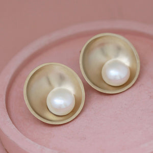 Gold pearl statement earrings shown on a pink ceramic dish
