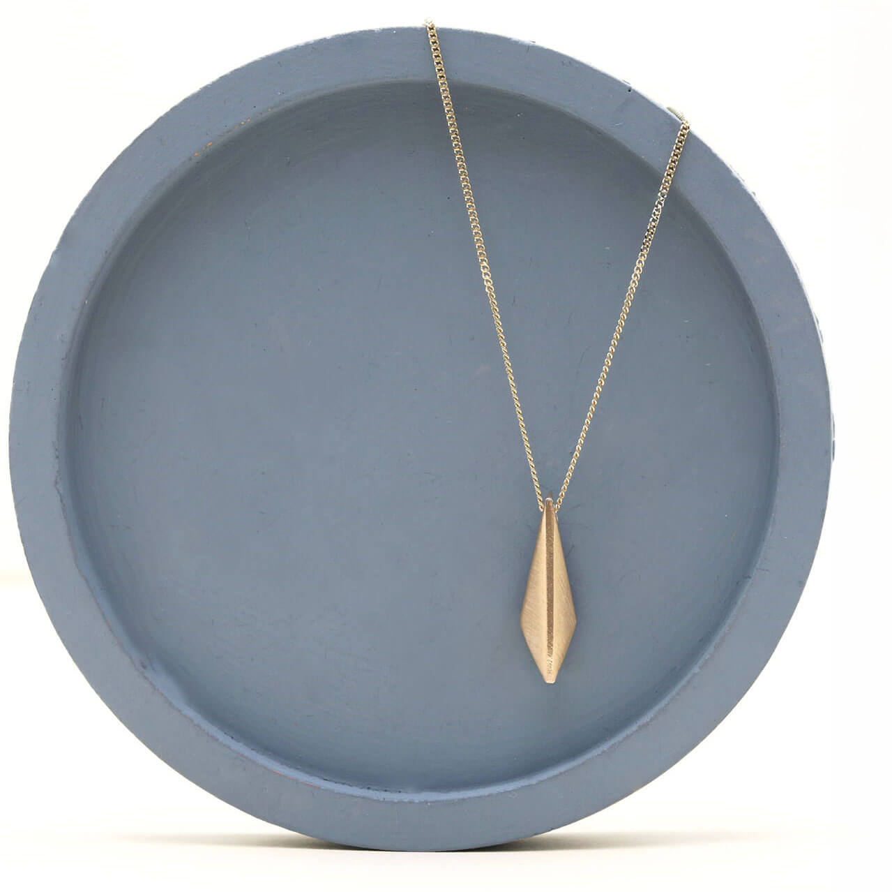9ct gold pendant for women with a polished geometric kite shape, photographed on a deep blue dish