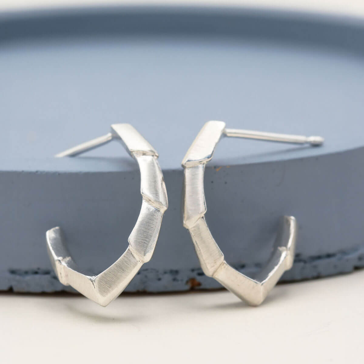 Half hoop earrings in polished sterling silver, showing the open geometric design and sculptural shape