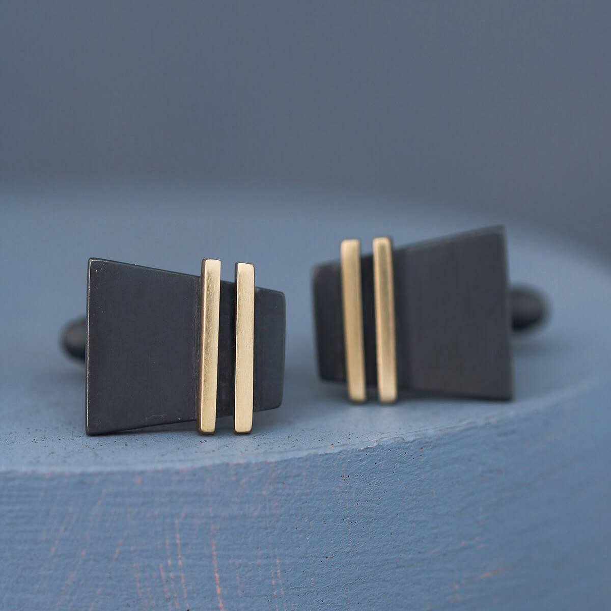 Single Black and Gold cufflink upright on deep blue background capturing gold stripe, an elegant pair of special cufflinks for milestone celebrations.