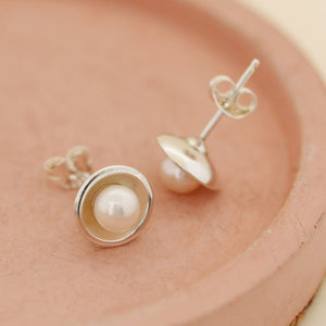 Pair of real pearl stud earrings resting on a blush pink dish, timeless Pearl Earrings for women with bright silver settings.