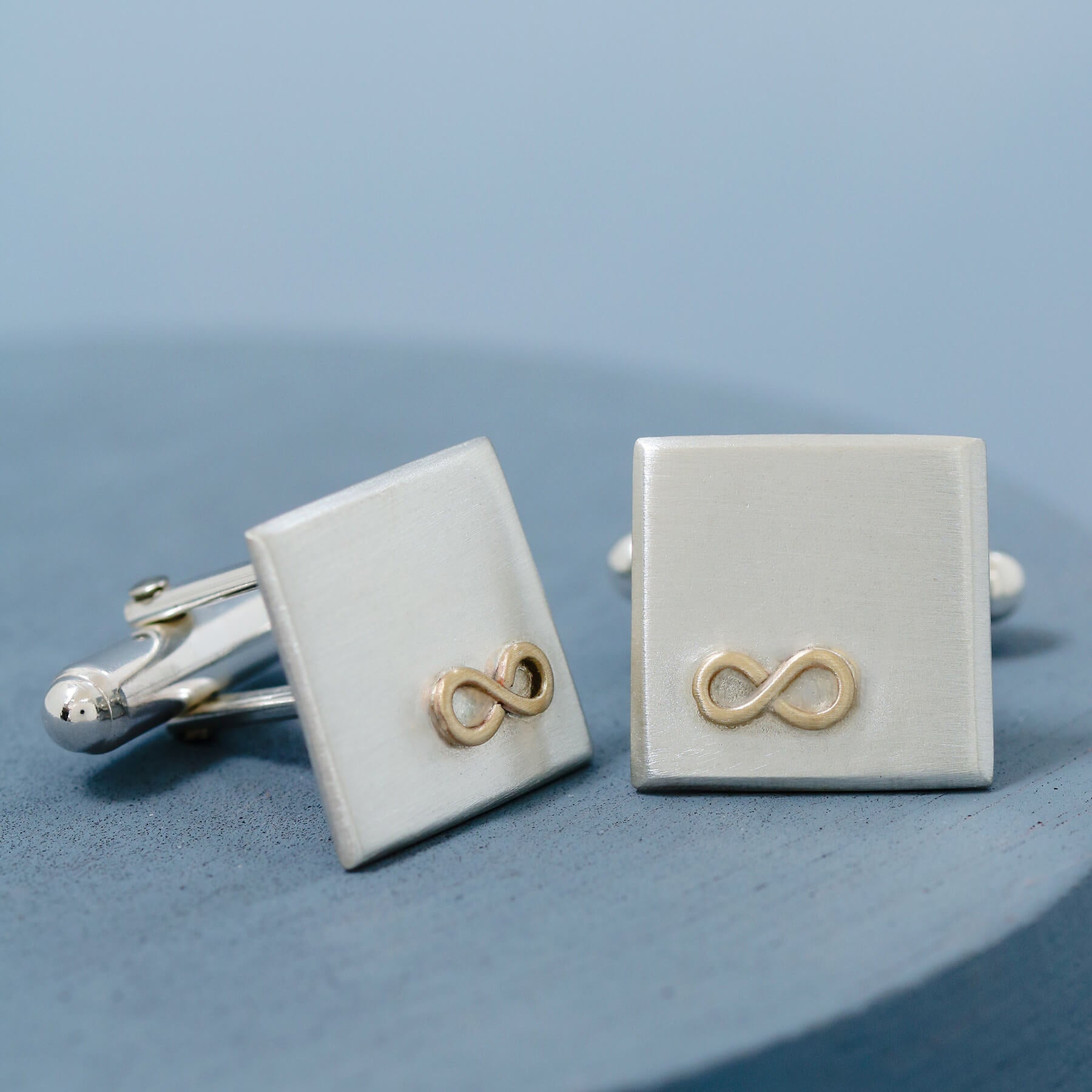 Gold and silver Cufflinks personalised, shown side by side on a deep blue background highlighting the geometric square shape and smooth finish.