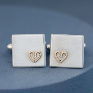 Pair of sterling silver cufflinks with a small 9ct gold heart on each, photographed on a deep blue background — Custom cufflinks for groom.