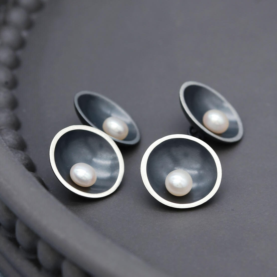 Black double-sided pearl cufflinks featuring freshwater pearls on both sides and a sterling silver chain connection.