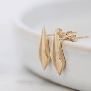 Polished surface of gold geometric earrings on pale grey, modern art deco bridal accessory.