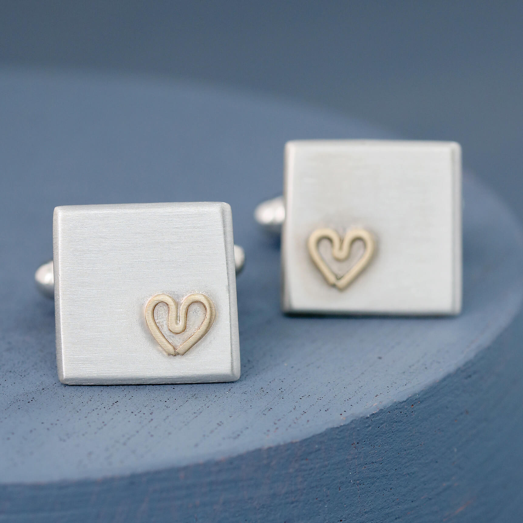 Both cufflinks positioned at an angle on a deep blue background showing their polished edges and heart motif — thoughtful gift for husband.