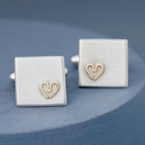 Both cufflinks positioned at an angle on a deep blue background showing their polished edges and heart motif — thoughtful gift for husband.