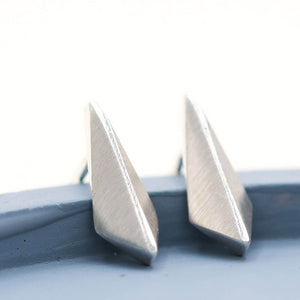 Plain silver stud earrings in a slim geometric kite design, photographed on a deep blue dish