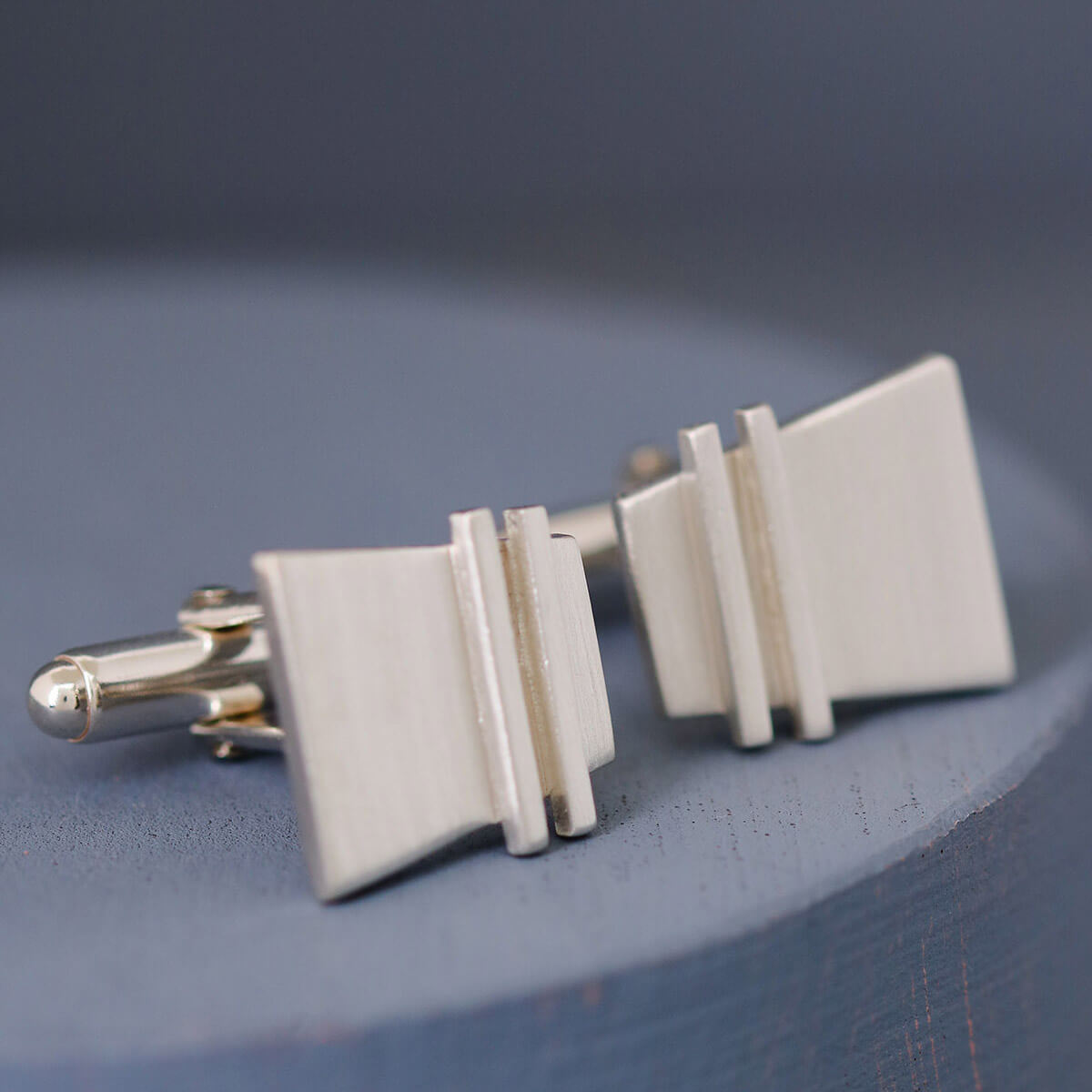 Close-up of Modern cufflinks highlighting geometric pinstripe texture and smooth silver finish, stylish and contemporary nice anniversary gift for husband.