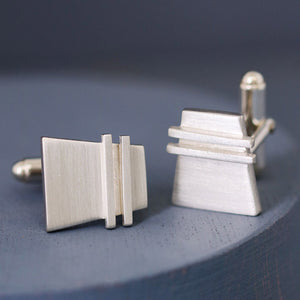 One cufflink face-on and one turned to show the back fitting, elegant handcrafted Modern cufflinks on deep blue background.
