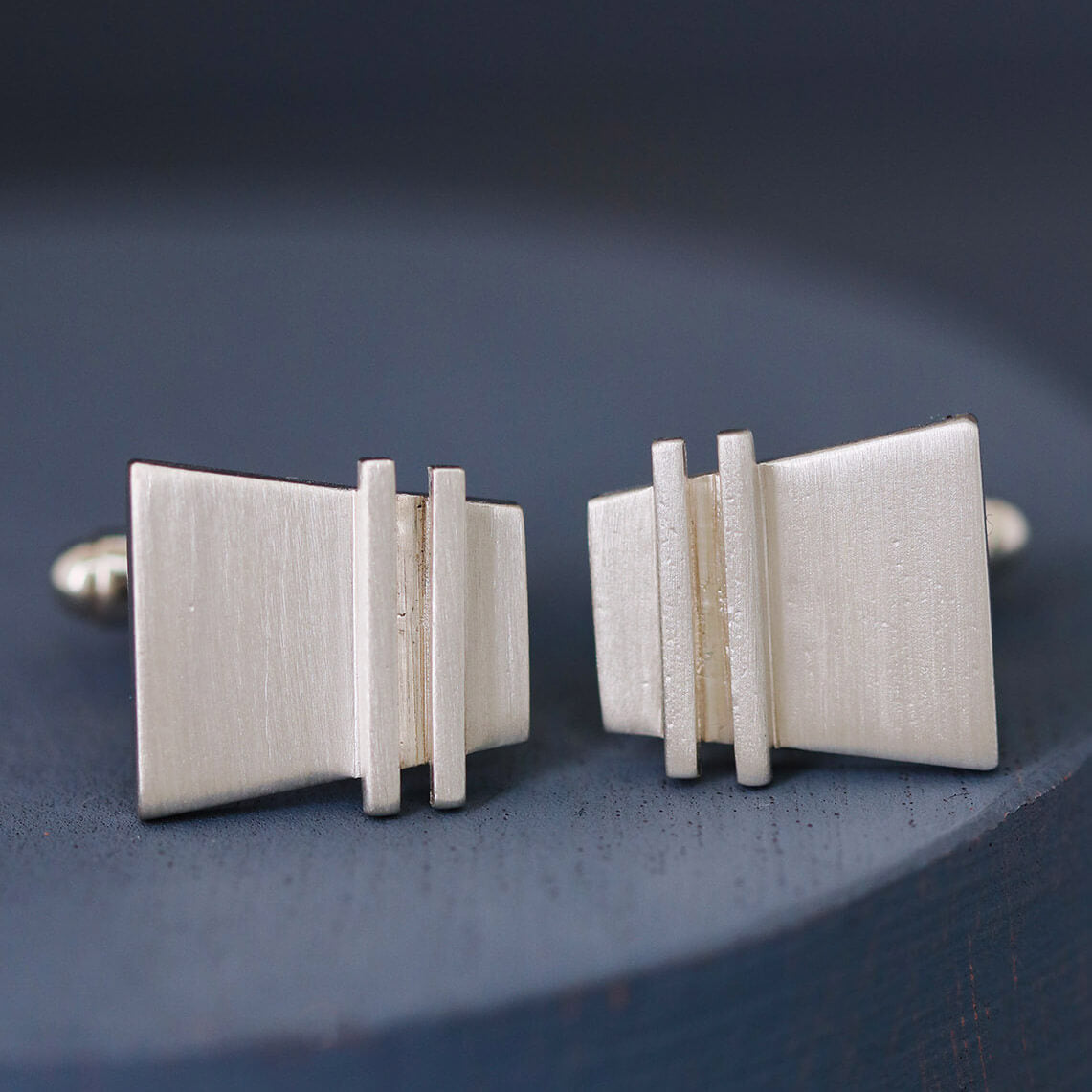 Modern cufflinks on deep blue background, showing minimalist geometric detailing and polished finish.