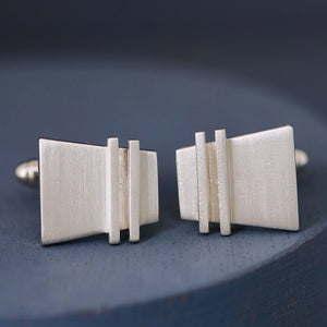 Modern cufflinks on deep blue background, showing minimalist geometric detailing and polished finish.