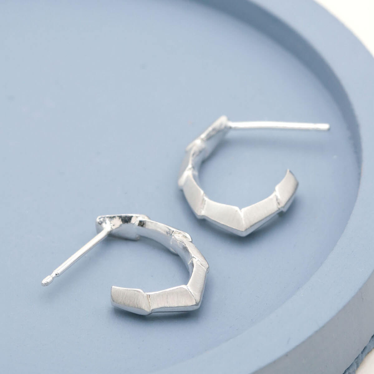 Solid silver hoop earrings with an Art Deco-inspired repeating pattern, photographed on a deep blue dish