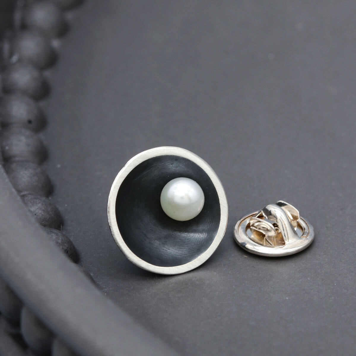 Close up of handmade black pearl tie pin showing the contrast between oxidised sterling silver and a genuine freshwater pearl.