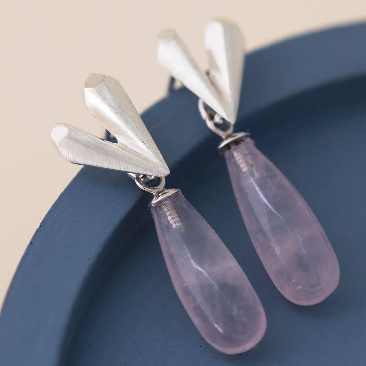 Pink heart earrings with faceted silver heart and teardrop rose quartz, heart dangle earrings laid flat on a blue dish