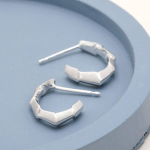Silver hoop earrings handmade in solid sterling silver, featuring a distinctive repeating geometric shape on a deep blue dish