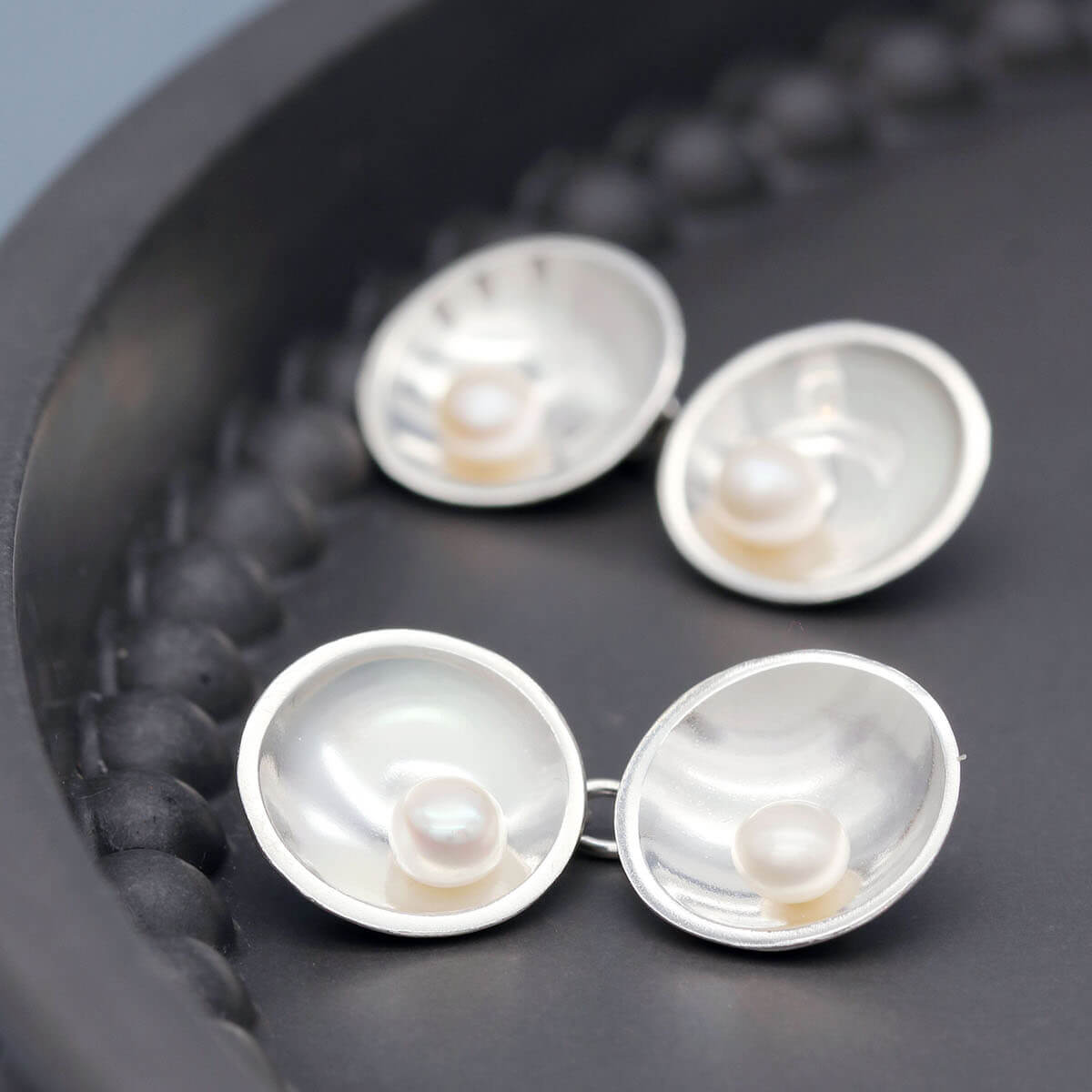Handmade sterling silver double-sided pearl cufflinks with genuine freshwater pearls displayed on a dark grey dish.