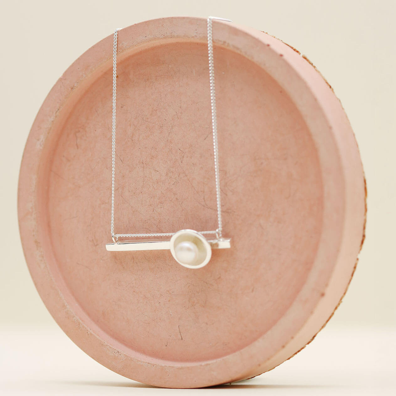 Close up of a sterling silver geometric pearl necklace highlighting the polished silver setting and natural freshwater pearl.