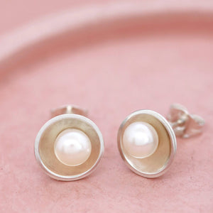 Close-up of pearl silver stud earrings on a pink dish, one earring turned up to show the comfortable stud fitting.