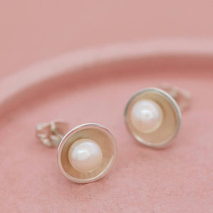 Side angle of pearl silver stud earrings on pink dish, highlighting the dome design and freshwater pearl centre.