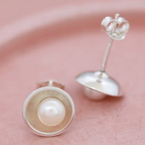 Sterling silver pearl stud earrings on pink ceramic dish, capturing the iridescent pearl in polished silver setting.