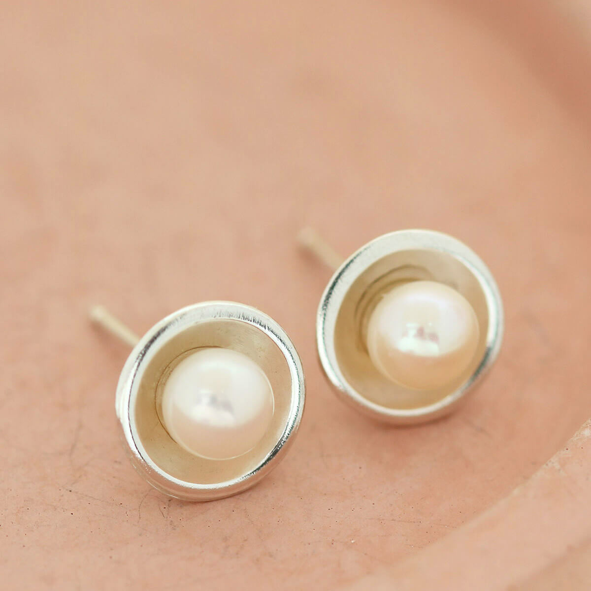 Minimal silver real pearl stud earrings placed on a pink dish, a classic pair of Pearl Earrings for women.