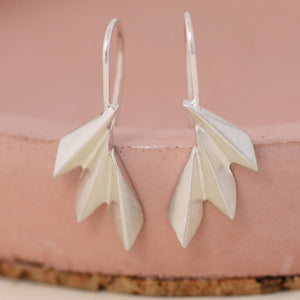 Art deco drop earrings resting on a pink ceramic dish with defined fan shapes catching the light; thoughtful Valentine’s gift for her.