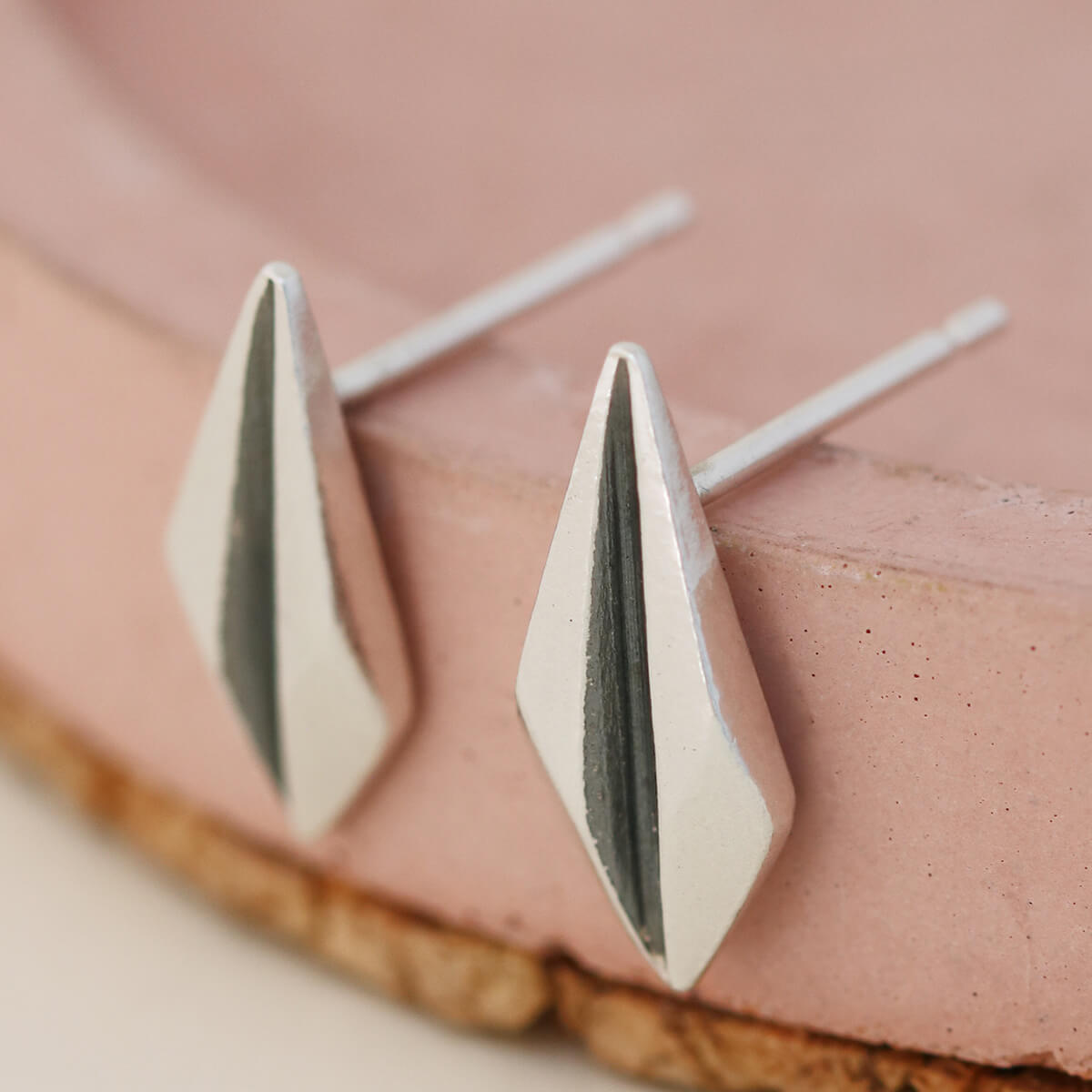 Silver art deco earrings displayed on a pink dish showing geometric design and oxidised detail.