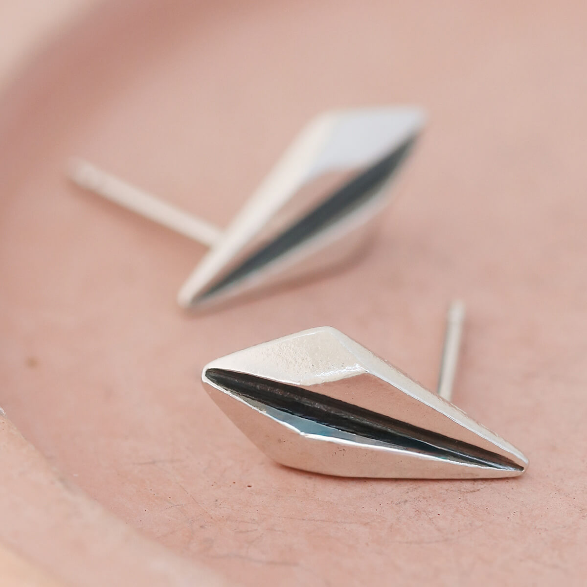 Close-up of silver art deco earrings on pink dish highlighting the ridged fan shape.
