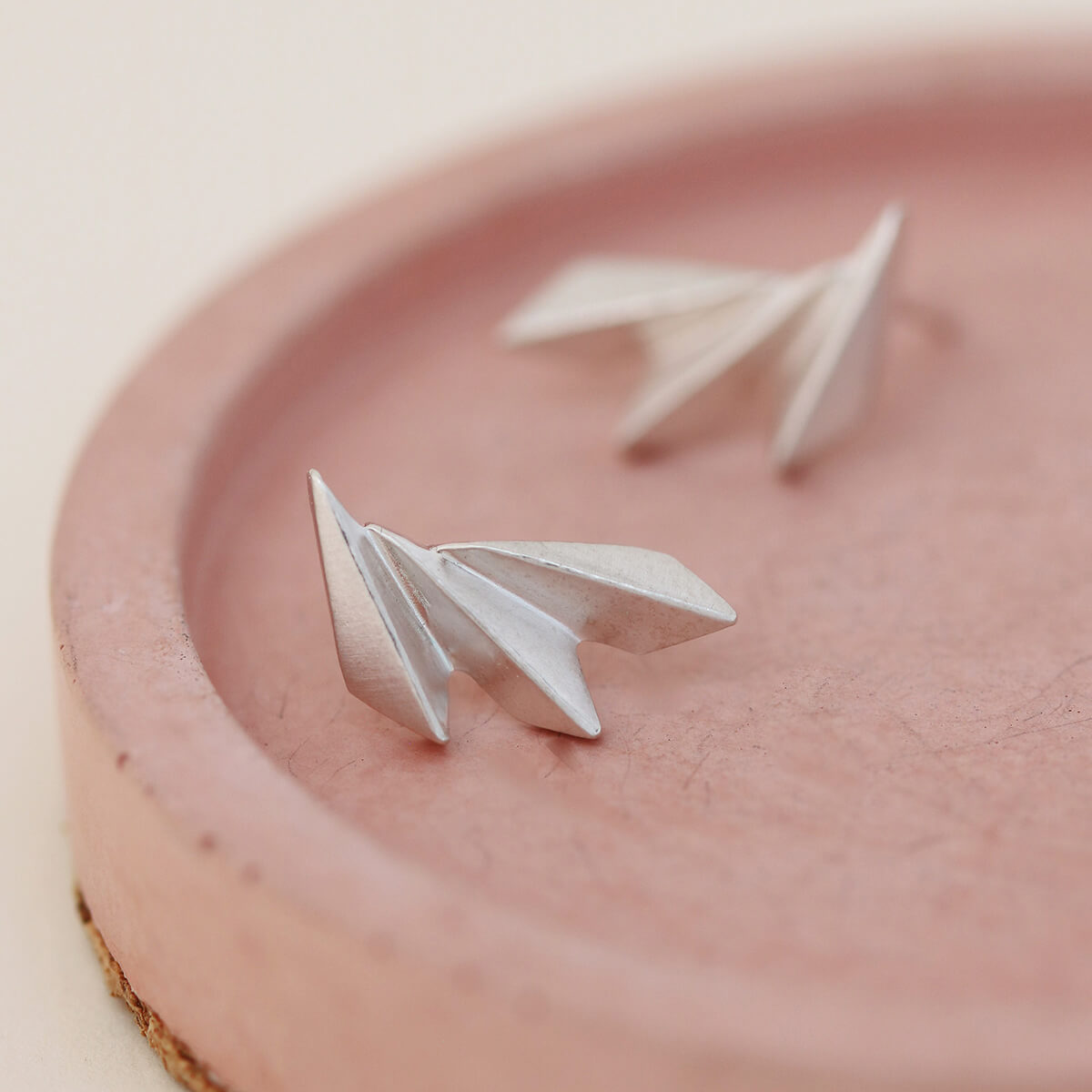 Art deco fan earrings on a pink dish with emphasis on the handcrafted shape.