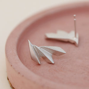 Pair of art deco silver earrings resting on a pink dish with soft natural lighting.