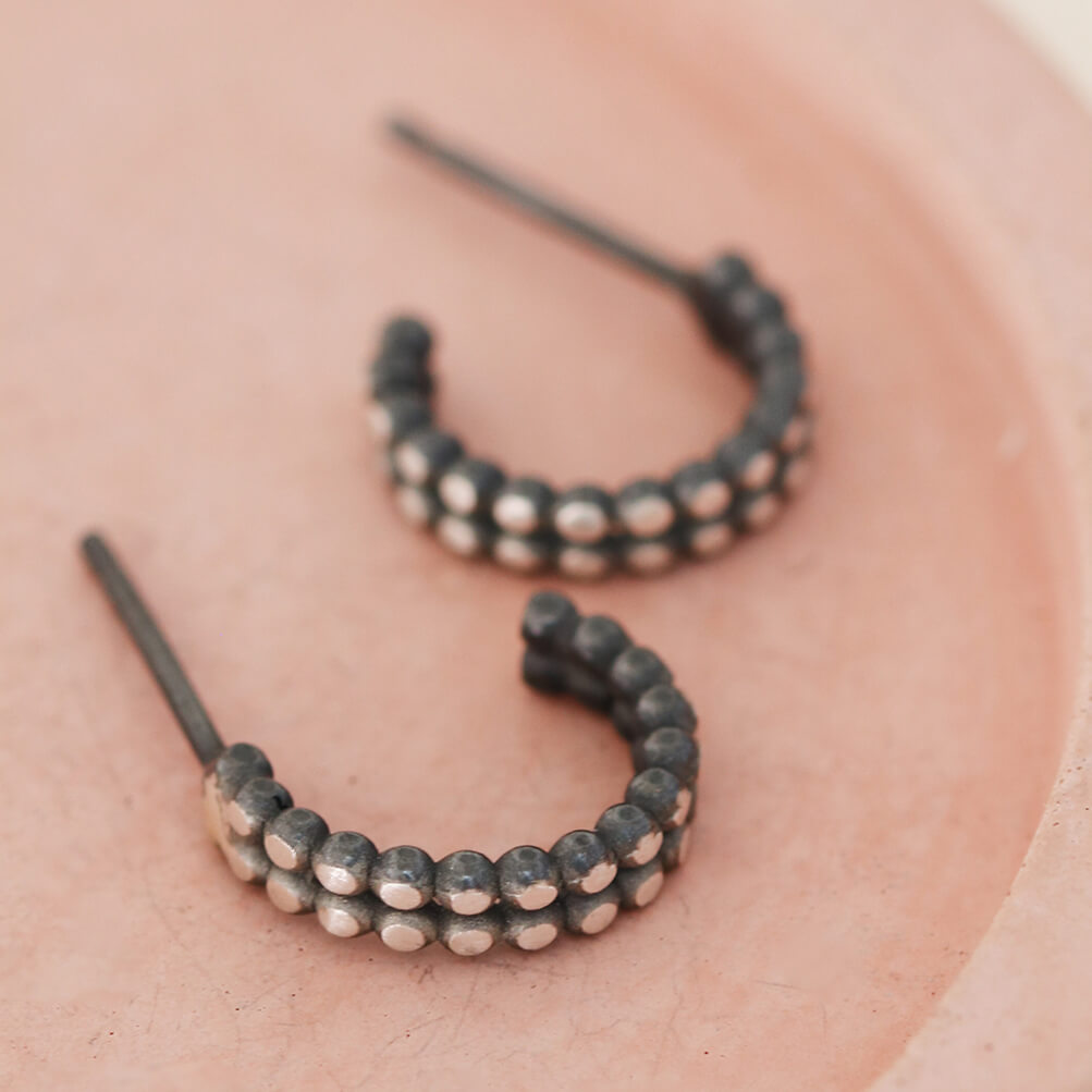 Sterling silver and black hoop earrings styled on a pink dish, small everyday huggie earrings
