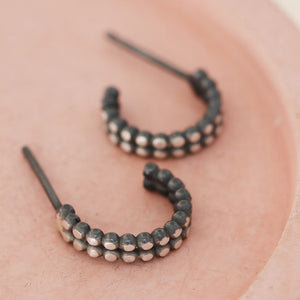 Sterling silver and black hoop earrings styled on a pink dish, small everyday huggie earrings