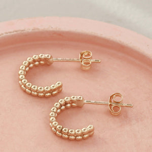 Close-up of small 9ct gold hoop earrings on a pink dish highlighting the textured beaded detail of these 9 carat gold hoops.