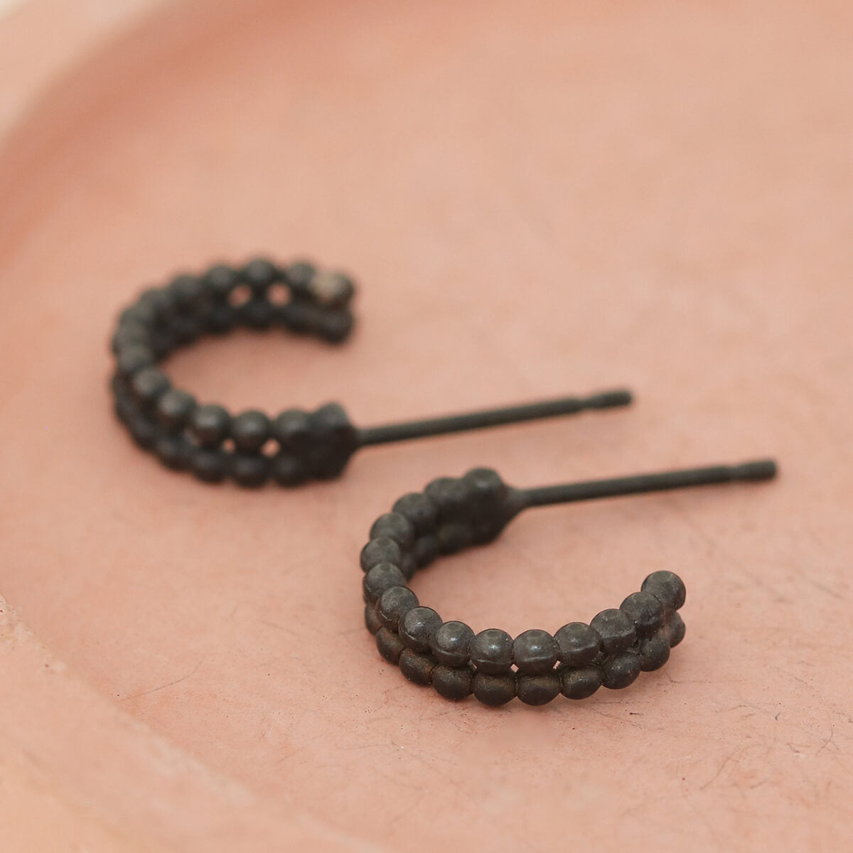 Black hoop earrings for women photographed on a pink dish, small black hoop earrings handmade in silver