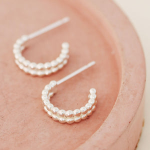 Small huggie hoop earrings in sterling silver displayed on a pink dish, minimalist double hoop beaded design