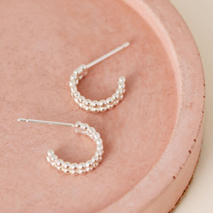 Close up of small huggie hoop earrings in sterling silver on a pink dish, everyday minimalist jewellery