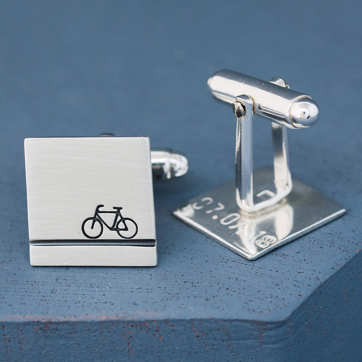 Pair of personalised bike cufflinks on a deep blue backdrop showing hand-stamped bicycle design, perfect cycling gifts for him for birthdays or weddings.