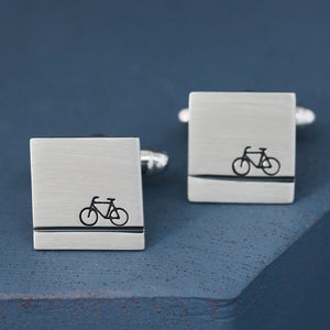 Close-up of silver bike cufflinks on deep blue background highlighting matte brushed finish, meaningful cycling gifts for him for anniversaries.