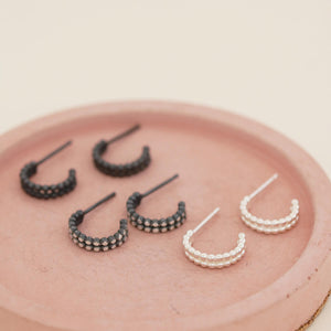 Small black hoop earrings shown with silver and black and silver finishes on a pink dish