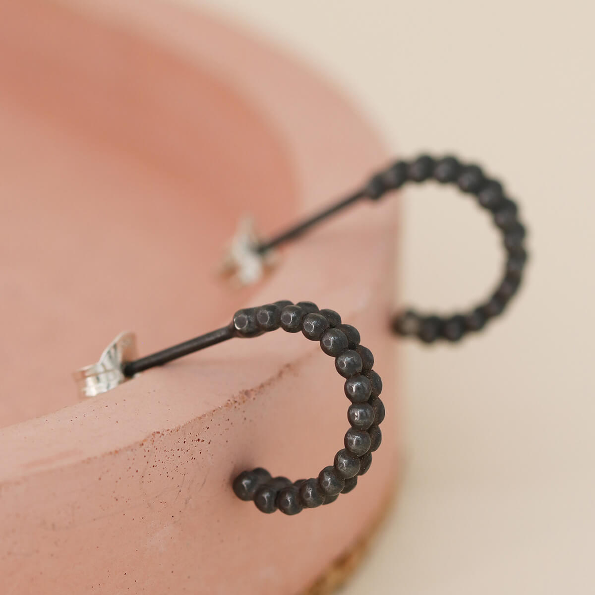 Close up of small black hoop earrings on a pink dish, modern minimalist black hoop earrings for women