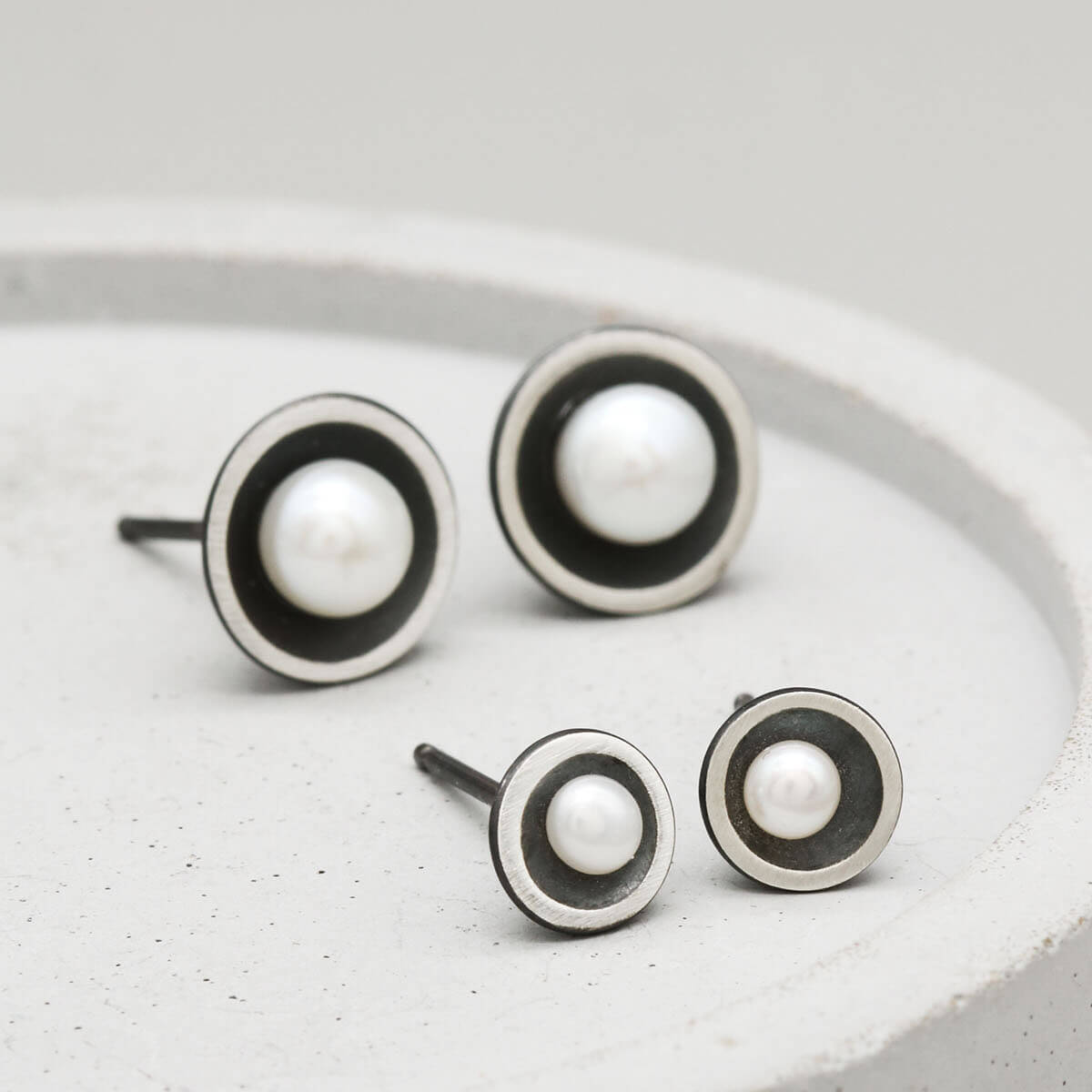 Small Petite pearl stud earrings displayed alongside the Classic size to highlight their delicate proportions.