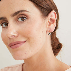 Black pearl hook earrings worn on the ear, showing the elegant floating profile created by the fixed sterling silver hooks. 