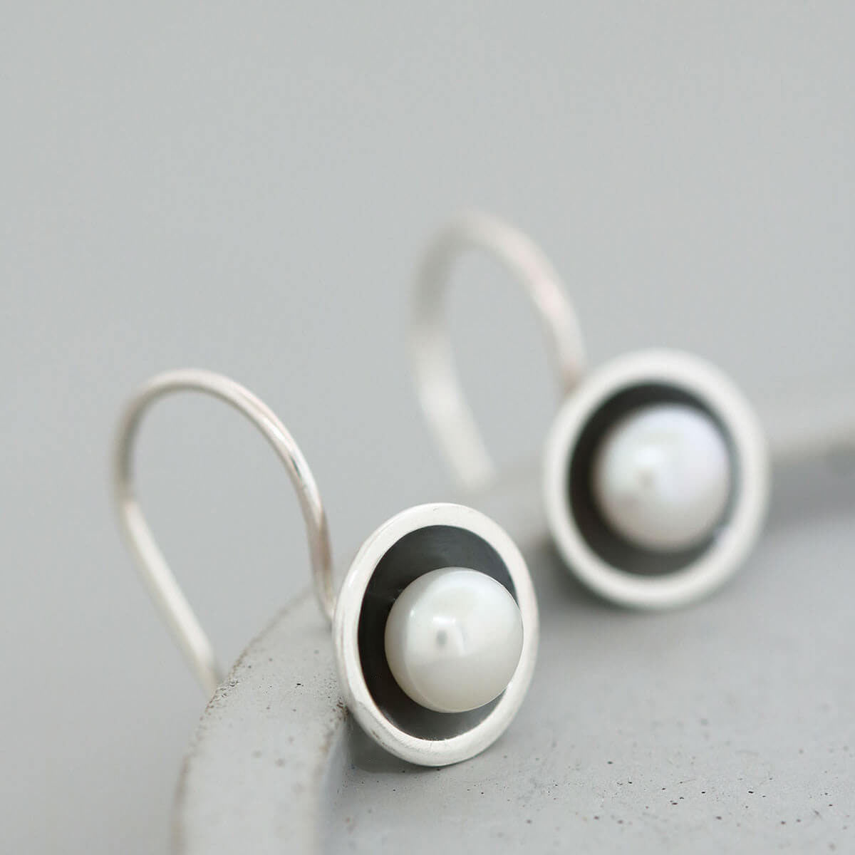 Handmade black pearl drop earrings with genuine freshwater pearls in oxidised sterling silver displayed on a grey ceramic dish.