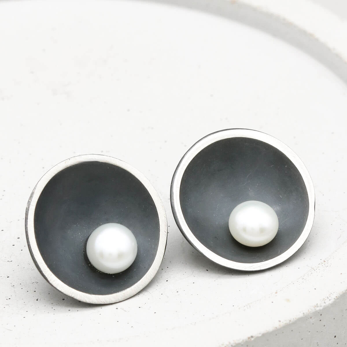Handmade Signature Black Pearl Stud Earrings in oxidised sterling silver with genuine freshwater pearls displayed on a grey ceramic dish.