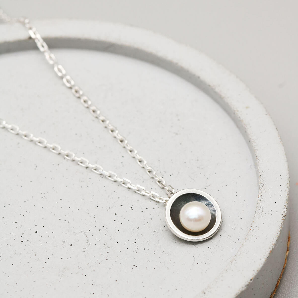 Handmade black pearl pendant necklace with a genuine freshwater pearl in an oxidised sterling silver setting on a dark grey dish.