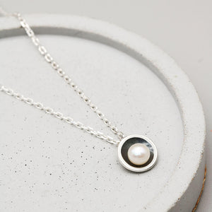 Handmade black pearl pendant necklace with a genuine freshwater pearl in an oxidised sterling silver setting on a dark grey dish.